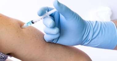 blued-gloved hand giving person injection in arm